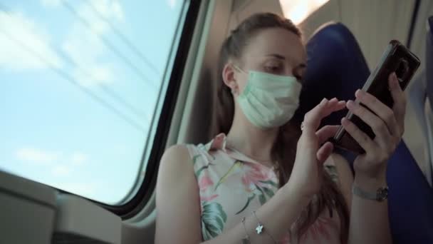 Female passenger feeling safety driving in local train and using medical protective face mask. Concentrated woman using smartphone, scrolling pages, reading social media news web sites and doing — Stock Video