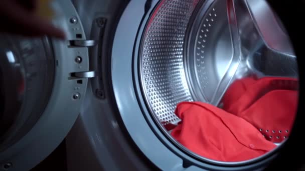 Gelbes Flüssiggranulat fließt in Zeitlupe in die Waschmaschine, Hausfrau belädt Elektromaschine mit verschmutzter Kleidung und füllt Waschmittelkapseln. Routinearbeiten im Haushalt, Wäsche waschen — Stockvideo