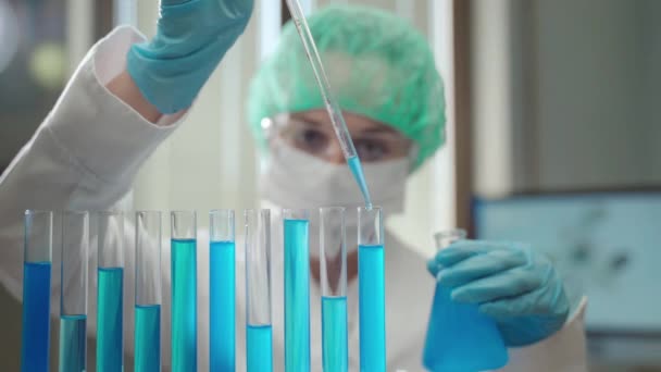 穿着医用防护服的女化学家研究人员在具有化学元素和不同试剂的病毒学实验室工作，实验室工作人员使用玻璃纤维无菌试验进行科学实验 — 图库视频影像