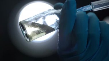 Close-up of potential vaccine in sterile glass vial on contrast background in researching laboratory, doctors hand holding bottle with vaccine solution and infusing liquid reagent with syringe