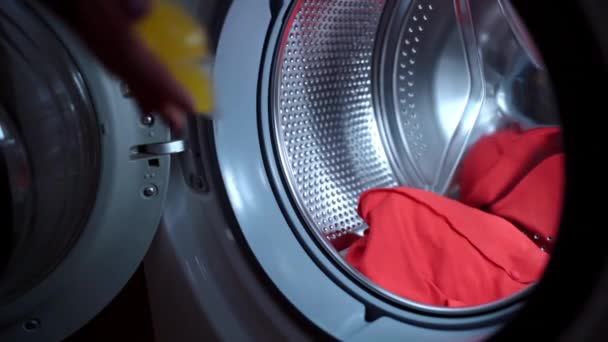 Gospodyni domowa rzucająca trzy chemikalia podwójnie skoncentrowane granulki detergentu w przezroczystą skorupę wewnątrz wirującego bębna pralki, proces załadunku brudnych ubrań do prania. zaciskacz ekologiczny oraz — Wideo stockowe