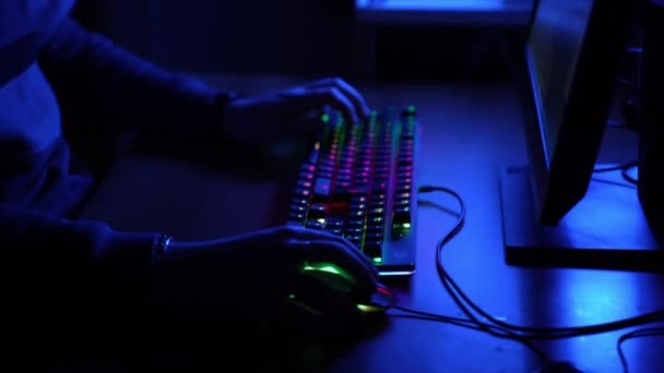 Pro gracz siedzi przy stole w ciemnoniebieskim oświetlonym biurze i grając w gry wideo online za pomocą podświetlanej klawiatury widma i myszy, haker komputerowy biorący udział w turniejach cyberprzestrzeni z — Wideo stockowe
