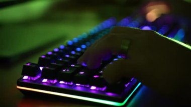 Sanal bilgisayar oyunları sırasında karanlık ofis odasındaki güçlü PC 'de sanal video oyunları sırasında profesyonel hacker tuşlara basarken RGB arka ışıklandırmalı klavye renk değiştiriyor. Modern teknolojide gökkuşağı tayfı