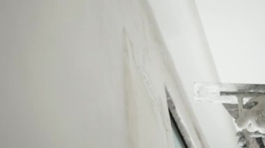 İnşaat alanındaki yeniden inşa edilmiş duvarın düşük açılı görüntüsü, yapı ustasının metal spatulayla duvara sürtünmesi ve hizalaması ve macun solüsyonunu bitirmesi. Duvarların beyazlatılması süreci