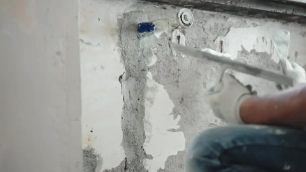 Réparateur qualifié en vêtements de travail écartelant vieux mur de ciment déchiqueté sous la fenêtre à l'aide d'une truelle métallique, d'une spatule et d'une pâte de plâtre blanche, surface du mur de nivellement par l'homme avec du stuc de mastic. Murs — Video