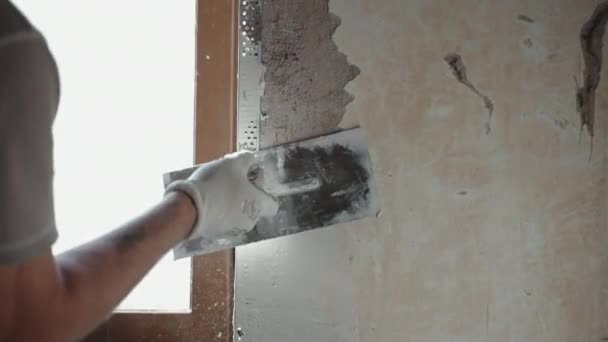 Professionele reparateur die werkt op de bouwplaats renovatie van een oud appartement. Bouwer met metalen spatel en witte klei pasta voor het pleisteren van binnenmuren en het dichten van cementgaten — Stockvideo