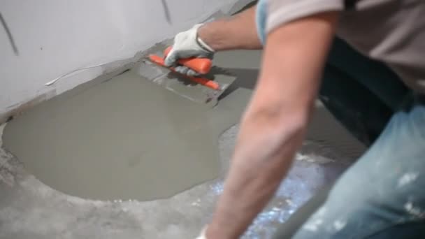 Engineering workman pouring self-leveling screed on floor, spreading it and smoothing with metal spatula, building master aligning fresh floor surface on construction site. Concrete mixture for floor — Stock Video