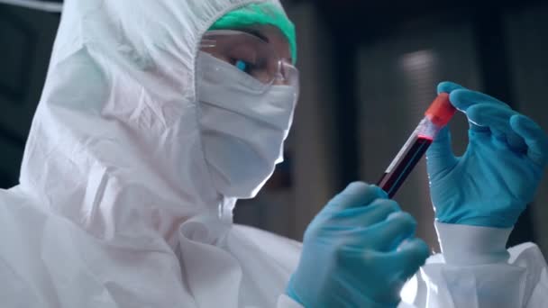 Laboratóriumi tudós védőburkolatban vérplazma kémcsövet tart a kezében és adatokat olvas. Fertőzött betegek vérplazmájának elemzése, laboratóriumi kísérletek a fejlődő — Stock videók