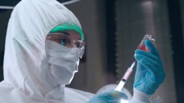 Bilimsel araştırma laboratuarında kimyasal deney, koruma altında biyofizikçi kırmızı rengin tehlikeli çözümü ile çalışıyor, şırıngayı şişeden dolduruyor ve test için hazırlanıyor.