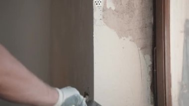 Koruyucu eldivenlerle inşaat işçisi macun duvarları için metal spatula kullanıyor, spatulayı macunla dolduruyor ve beton duvar yüzeyini kaplıyor. İnşaatçı duvar ve açıyı düzleştiriyor
