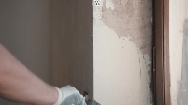 Будівельник в захисних рукавичках з використанням металевого шпателя для шпаклівки стін, ремонтант заповнює шпатель розрізною пастою і покриває поверхню цементної стіни. Будівельник вирівнювання стіни і кута біля — стокове відео