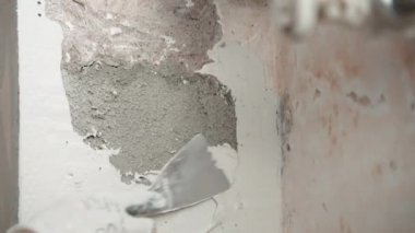 İnşaat alanındaki tamamlanmamış beton duvarın yakın çekimi, sıva sıva kullanan metal spatula, alçı sıva ile kaplanmış duvar ve açılar. Oyuncak duvarlar, apartman onarımı, tamirat.