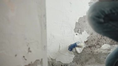 Metal mala, spatula ve beyaz macun kullanarak beton duvarları sıvayan, duvar yüzeyini macun kaplamalarıyla düzleştiren ve hizalayan bir adam. Duvarların yenilenmesi, tamirat konsepti