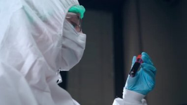 Mikrobiyoloji ve viroloji konsepti. Koruyucu kılıf üzerinde çalışan laboratuvar bilim adamı elinde kan plazma test tüpü tutuyor ve araştırma verilerini okuyor. Hastalıklı hastaların kan plazmasının analizi