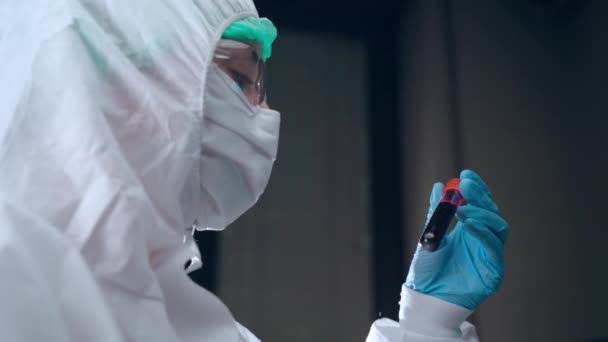 Conceito de microbiologia e virologia, cientista de laboratório em macacão protetora segurando tubo de teste de plasma sanguíneo em mãos e lendo dados de pesquisa. Análise do plasma sanguíneo de doentes infetados — Vídeo de Stock