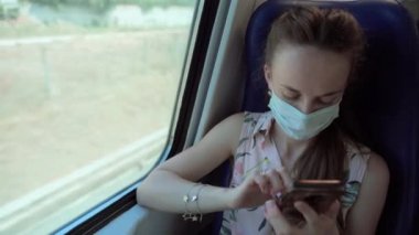 Koruyucu yüz maskeli kadın trenle seyahat ediyor ve internet üzerinden alışveriş yapıyor. Akıllı telefon ve uygulamalar kullanıyor. Kadın yolcu internette geziniyor.