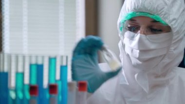 Tıbbi araştırmacılar laboratuarda bulaşıcı enfeksiyonlara karşı aşı deneyleri yapıyorlar. Koruyucu kılıflı kadın virüs uzmanı elinde potansiyel bir aşı şişesi tutuyor ve onu sallıyor.