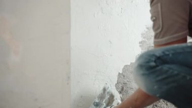 Metal mala, spatula ve beyaz sıva macunu kullanarak beton duvarları ve açıları alçılayan, duvar yüzeyini macunla kaplayan bir adam. Duvarları yenileme, yenileme konsepti