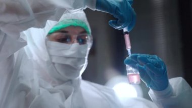 Laboratuvar araştırmacısı steril şişeye toz ve sallanan reaktif çözeltisi yerleştiriyor. Koruyucu örtüde biyofizikçi araştırma laboratuarında tehlikeli çözeltilerle çalışıyor.