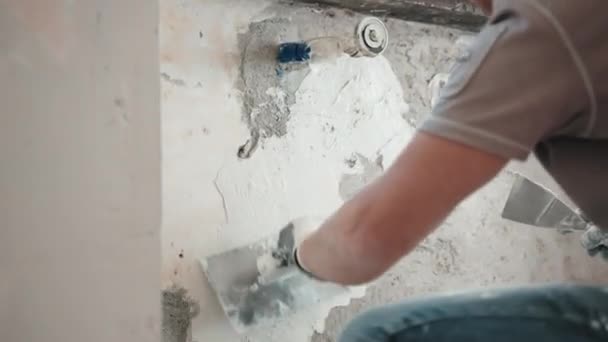 Мужчина-строитель оштукатуривает цементную стену шпаклевкой, металлическим шпателем и лопаткой. Рабочий выравнивает неровную стену в новой квартире на строительной площадке, выравнивая структуру стен профессиональными инструментами — стоковое видео