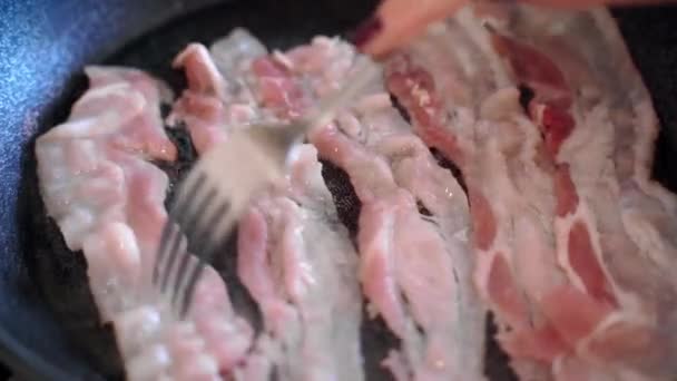 Dona de casa usando garfo e dividindo tiras de bacon de fritura na superfície da panela quente, assando fatias de carne para o café da manhã ou almoço. Processo de preparação de alimentos não saudáveis, conceito de junk food — Vídeo de Stock