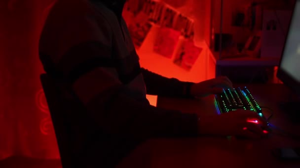 Sala oscura iluminada con luces de neón rojas y hacker profesional jugando juegos de video en línea día y noche. Primer plano de las personas dedos haciendo clic en el teclado de la computadora con iluminación retroiluminada espectro. Vídeo — Vídeos de Stock