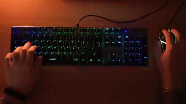 Vista superior das mãos dos jogadores digitando no teclado do computador com iluminação retroiluminada RGB e clicando no mouse do computador iluminado. Pro gamer jogar jogos de vídeo cibernéticos em casa, conceito de entretenimento de tecnologia — Vídeo de Stock