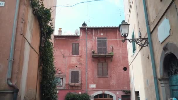 Камера движется по старинной характерной улице старой деревни Тоскана в провинции Витербо, величественная уличная атмосфера при дневном свете со старым фасадом здания разного цвета. Высокая жилая — стоковое видео