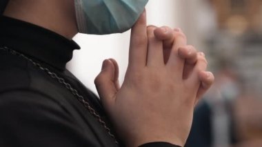 Koruyucu yüz maskeli rahibe kutsal ayin sırasında el ele tutuşup dua ediyor. Kilisenin arka planında dua eden dindar kardeşlerin elleri kesişiyor. Siyah cüppeli Hıristiyan.