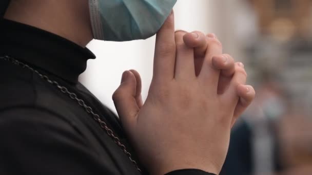 Монахиня в защитной маске для лица скрещивает руки и молится в церкви во время святой мессы, крупным планом религиозных сестер руки скрещены на размытом церковном внутреннем фоне. Кристиан в черной рясе — стоковое видео