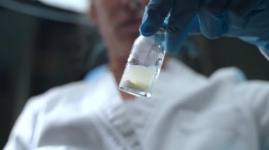 Laboratuvar araştırmacılarının elindeki potansiyel aşı şişesinin düşük açılı görüntüsü, profesyonel virüs uzmanı şişeyi sallıyor ve bileşik reaksiyonu izliyor. Elementler ve çözümlerle yapılan kimyasal deneyler