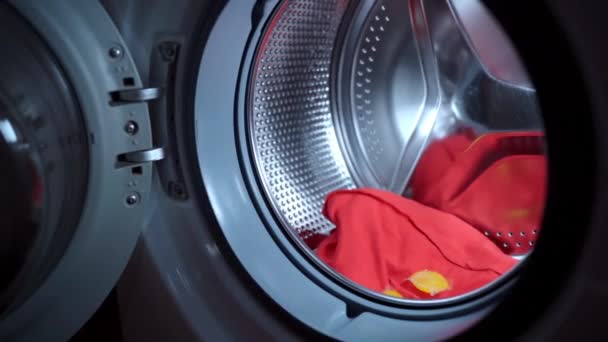 Chemisches Flüssiggranulat zur Beseitigung von Flecken auf verschmutzter Kleidung, Frau lädt elektrische Waschmaschine mit rotem, verschmutztem Tuch und wirft Flüssigwaschmittel. Vorbereitung der Waschmaschine, Wäschekonzept — Stockvideo