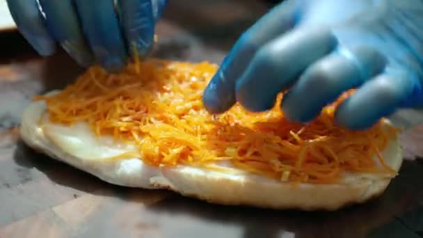 Готовим сэндвич с фаст-фудом, шеф-повар в перчатках набивает горячую булочку с пряными ломтиками моркови на доске. Вкусная готовая еда, уличная еда и концепция нездорового питания — стоковое видео