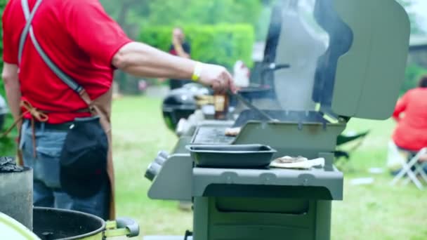 Pessoas comemorando churrasco de fim de semana ao ar livre, homem assando variedade de carne na grade de churrasco e usando pinças de cozinha para verificar a prontidão da carne suculenta. Piquenique de churrasco na natureza — Vídeo de Stock