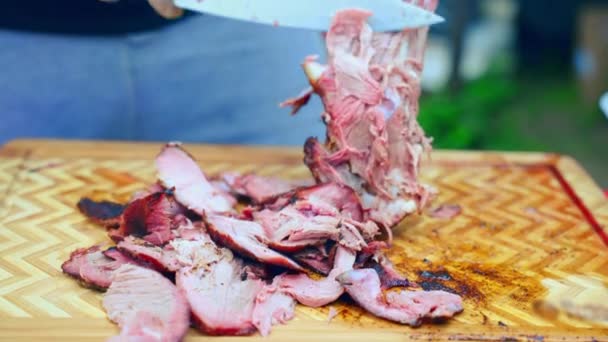 Chef em luvas de cozinha estéreis cortando assado perna de cordeiro suculento na placa de madeira esculpida usando faca de cozinha, homem cortando osso de cordeiro picante em pedaços preparando prato de carne para a festa de churrasco. Cordeiro grelhado — Vídeo de Stock