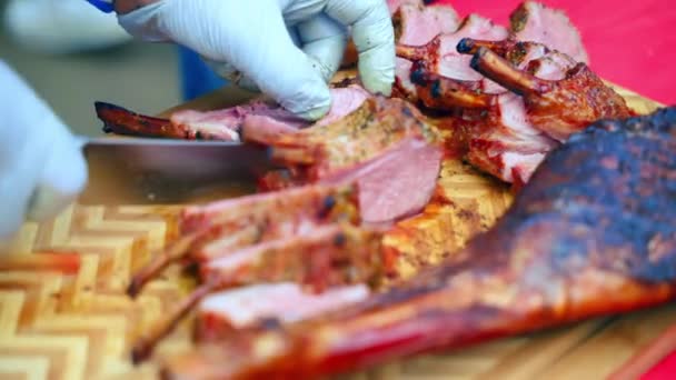 Close-up shot van chef-kok met keukenmes voor het snijden van sappige lamsribben op stukken en het snijden van lamsbout op traditionele barbecue festival, half-afgewerkt lamsvlees roken op houten snijplank buiten — Stockvideo