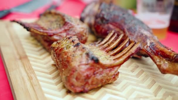 Hot rack of crispy lamb ribs on wooden cutting board on bbq picnic party, juicy smoking lamb meat in close-up. Mouth-watering lamb ribs roasted on barbecue grill grid on charcoals flames, prime sort — Stock Video