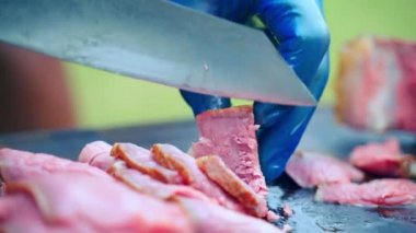 Izgara sığır filetosu dilimleme işlemini yakından çek, kauçuk eldivenli şef orta pişmiş dana filetosunu kesme tahtasında kes. bbq yemek yemeklerini piknik partisi için hazırlamak, et kızartmak.