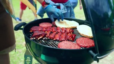 Barbekü partisi açık havada, insanlar lezzetli ızgara et tatmak için toplanıyor bbq ızgarasında kızartılıyor. Çiğ hamburger, erimiş peynirli çörekler ve baharatlı domuz pirzolası.