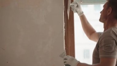 İnşaat işçisi inşaat alanındaki sıva işleri için profesyonel aletler kullanıyor, duvar yüzeyini metal spatula ve macunla hizalayıp düzleştiriyor. Mühendislik endüstrisi