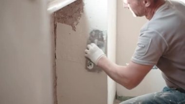 Çalışan giysiler içinde tamirci pencerenin altına metal mala, spatula ve beyaz macun kullanarak eski püskü beton duvarları kokutuyor, duvar yüzeyini macun kaplamasıyla düzleştiriyor. Duvarların yenilenmesi