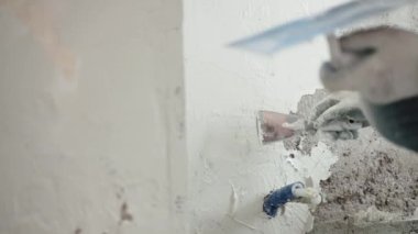 Metal mala, spatula ve beyaz macun kullanarak beton duvarları sıvayan, duvar yüzeyini macun kaplamalarıyla düzleştiren ve hizalayan bir adam. Duvarların yenilenmesi, tamirat konsepti
