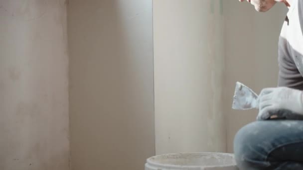 Reparateur zetten oude rafelige cement muur onder het raam met behulp van metalen troffel, spatel en witte spackling pasta, man egaliseren muur oppervlak met stopverf stucwerk. Muren restauratie, revisie concept — Stockvideo
