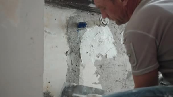 Naprawiacz szybuje starą poszarpaną ścianę cementową pod oknem metalową kielnią, szpachelką i białą pastą tynkarską, człowiek wyrównuje powierzchnię ściany szpachlówką. Remont ścian, koncepcja remontu — Wideo stockowe
