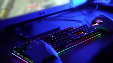RGB arka ışıklandırmalı bilgisayar klavyesi eğlence, eğlence ve çevrimiçi video oyunları oynamak için. Fareye tıklayarak ve klavyede mavi ışıkta geçerek yazı yazan insanların yakın plan görüntüsü