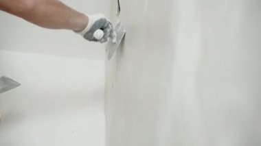 Koruyucu eldivenlerle duvarları metal spatulayla kaplayan, duvar yüzeyini beyaz alçı macunu çözeltisiyle düzenleyen ve hizalayan bir mühendis. Duvar beyazlatma işlemi, onarım