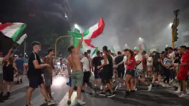 ローマ,イタリア- 2021年7月11日: UEFA EURO 2020でサッカーチームの勝利後の道路をブロックするフラグを振ってイタリアのファン、路上で踊る幸せなストリートファン、ジャンプや喜びで叫んで — ストック動画