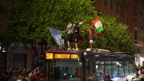 ROMA, ITÁLIA - JULHO 11, 2021: Bêbado rua engraçado hooligans italianos com bandeiras dançando no telhado do ônibus, pulando e gritando, multidão de pessoas bloqueando o transporte de passagem nas ruas de Roma. Fãs de futebol — Vídeo de Stock