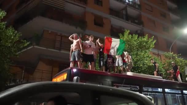 ROMA, ITÁLIA - JULHO 11, 2021: Bêbado rua italiano hooligans no telhado de ônibus dançando, gritando, agitando bandeiras, pulando e levantando as mãos para cima, caras apoiando equipe esportiva italiana com multidão após a vitória — Vídeo de Stock