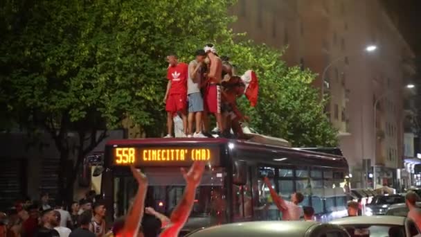 ROME, ITALY - JULY 11, 2021: Drunk funny street Italian hooligans with flags dancing on bus roof, jumping and shouting, crowd of people blocking passing transport on the streets of Rome. Football fans — Stock Video